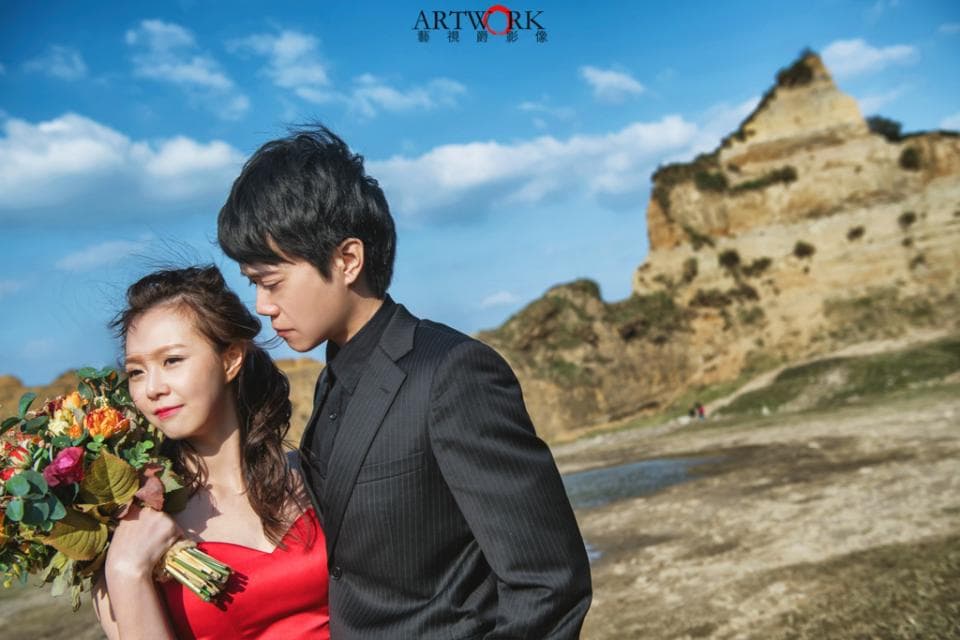 這張「婚紗照」的照片是一對新人站在黃土色的山坡前,新郎穿著黑色西裝,新娘穿著紅色禮服,他們手上都拿著鮮花,看起來非常甜蜜幸福。