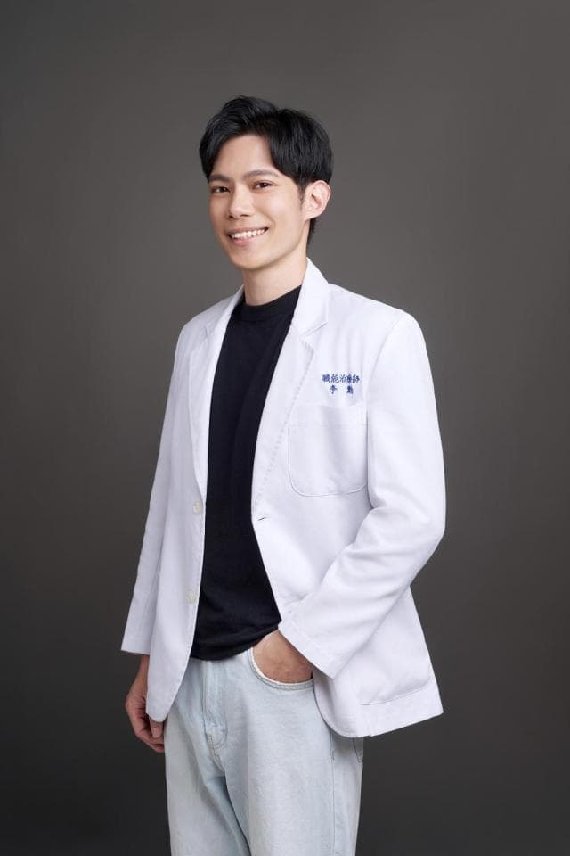 這張照片是一個穿著白色外套的男性,他穿著黑色上衣和淺色牛仔褲,手插在口袋裡,面帶微笑,看起來很自信。