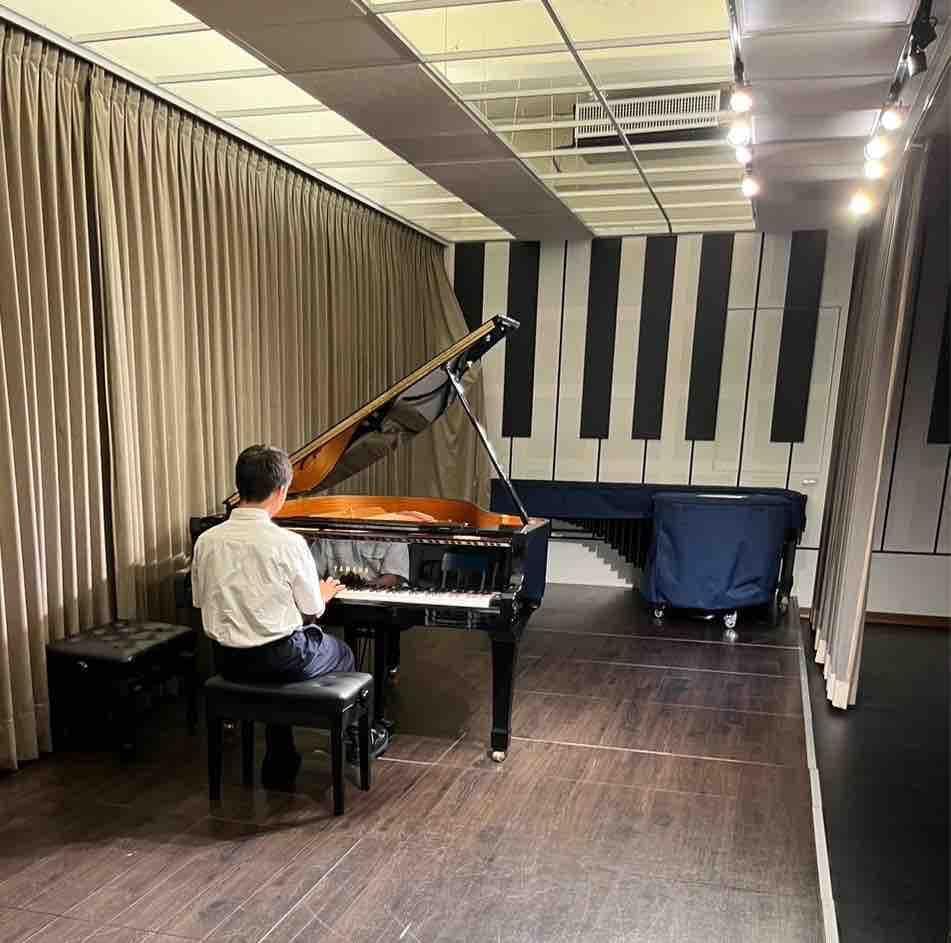 這張照片是一個練習室,裡面有一位男士正在彈鋼琴。