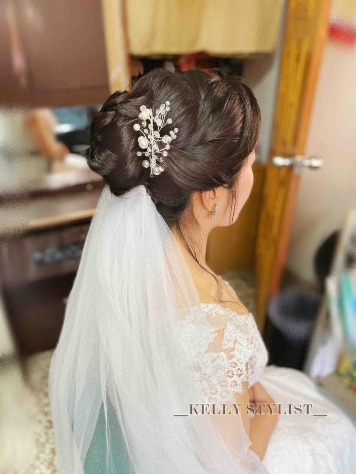 這張「新娘」的照片是一位戴著頭紗,穿著蕾絲婚紗的女性,她正在做婚禮造型,髮型是優雅的盤髮,頭上戴著珍珠髮飾。