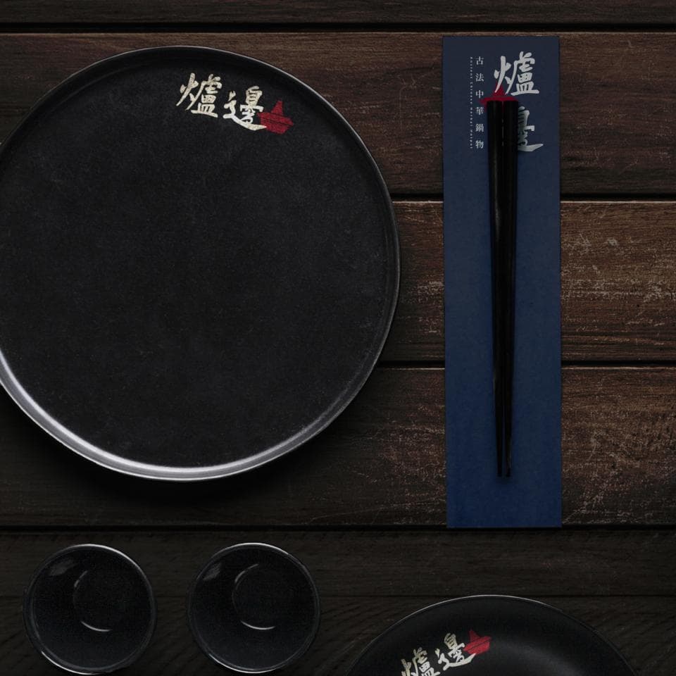 這張照片是一張木製背景上的黑色餐盤和藍色餐墊,餐墊上放著一雙黑色的筷子。