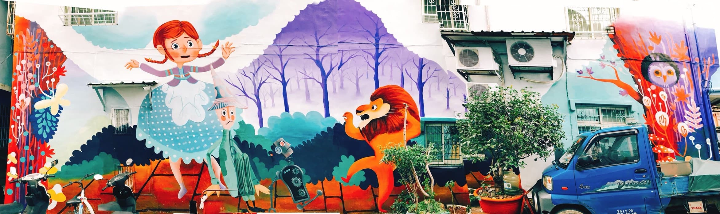 這張「牆壁上的塗鴉」的照片是,一位紅頭髮女孩走在森林裡,一隻獅子在她身旁,旁邊還有其他的塗鴉,包括一輛藍色的卡車。