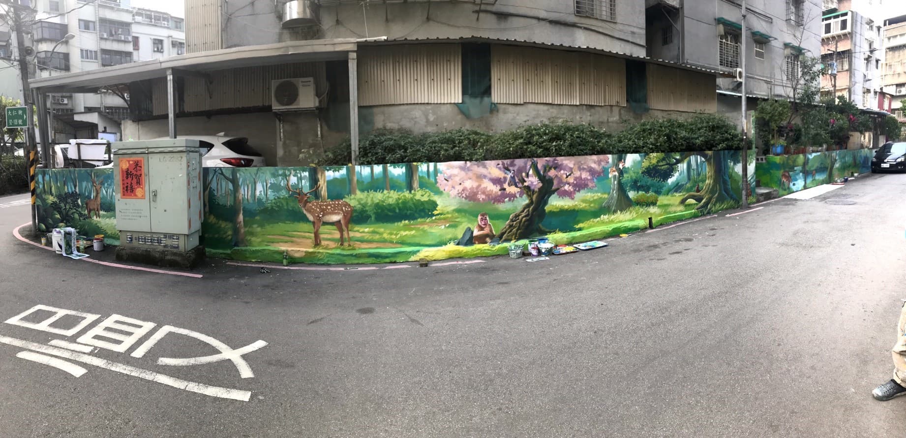 這張「牆上繪畫」的照片是一幅以森林為主題的壁畫,上面有樹木、動物和人物,讓原本單調的牆面變得充滿生機。