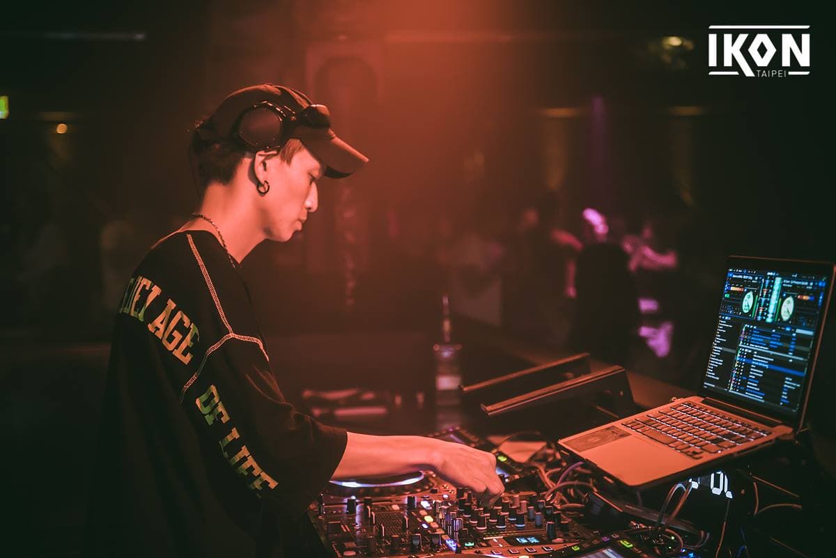 這張「DJ 在音樂節現場表演」的照片是,一位 DJ 戴著耳機,正在操作混音器,現場有很多人在跳舞。