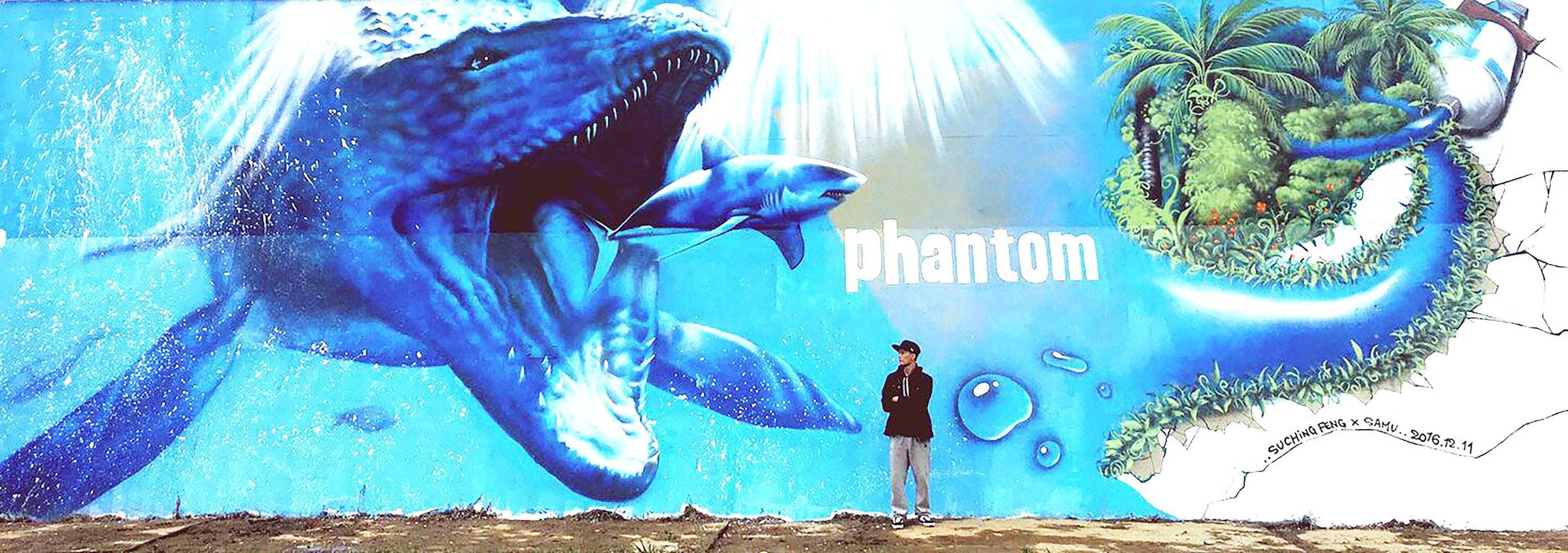 這張照片是一個巨大的鯨魚壁畫,牠張開了嘴,露出鋒利的牙齒。鯨魚的尾巴被畫成一個環,圍繞著一棵棕櫚樹。