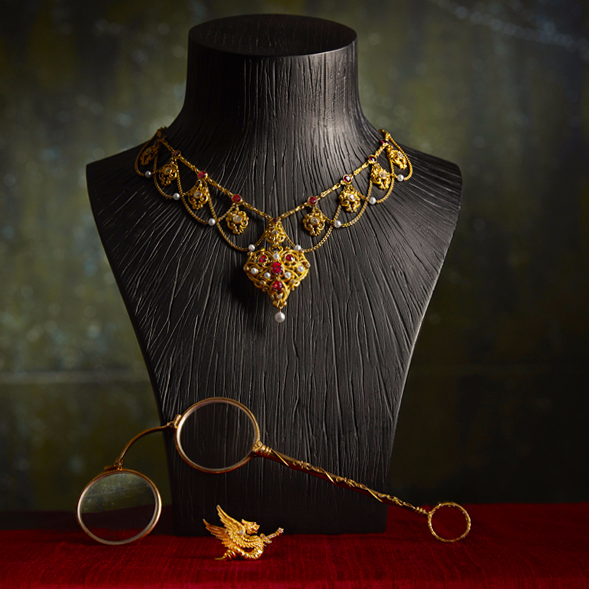 這張照片是一條金色項鍊,它由紅寶石和珍珠組成,項鍊掛在一個黑色的木質底座上。