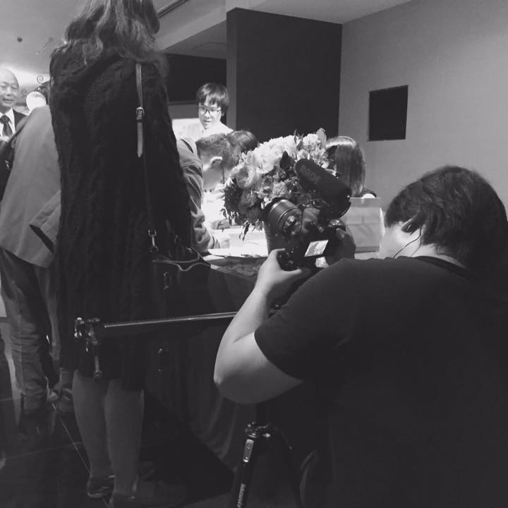 這張照片是一個攝影師正在拍攝一群人。他拿著攝影機,手裡拿著話筒,似乎正在採訪他們。