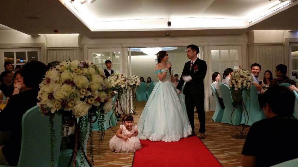 這張照片是婚禮現場,一對新人正在臺上交換誓言。新郎穿著黑色西裝,新娘穿著白色婚紗,他們都面帶笑容,看起來十分幸福。