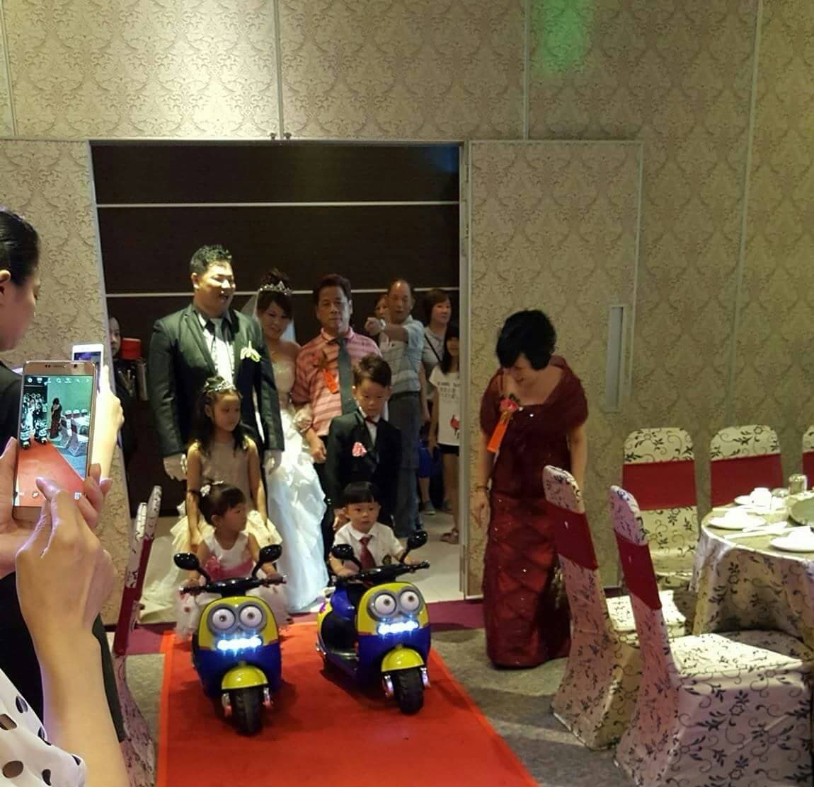 這張婚禮的照片是一對新人和他們的小朋友們,小朋友們騎著可愛的摩托車在紅地毯上。