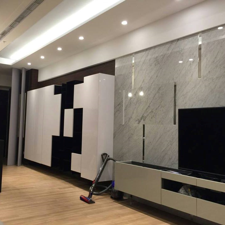 這張照片是一間客廳,最重要的是牆上的電視櫃。電視櫃是由白色大理石打造,配上幾條銀色的線條,電視櫃下方有一個黑色的電視,櫃子旁邊有一個吸塵器。