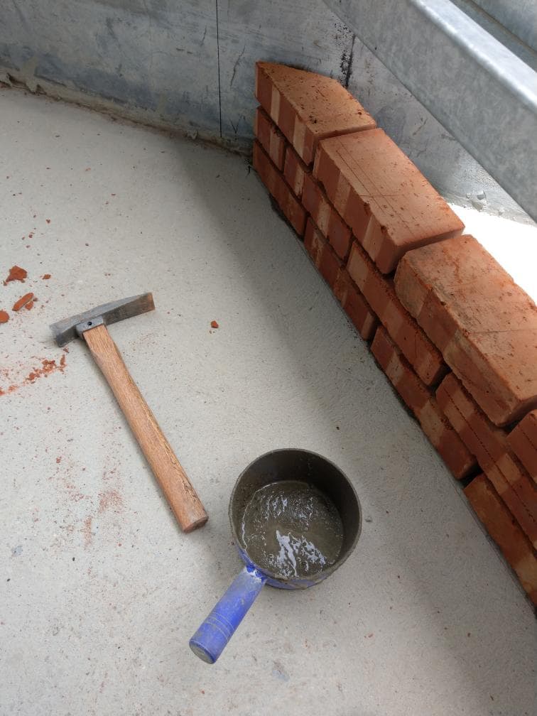 1) 照片顯示一個水泥地板上有一堆紅磚,旁邊放著一把木柄鎚子和一個藍色手柄的鍋子