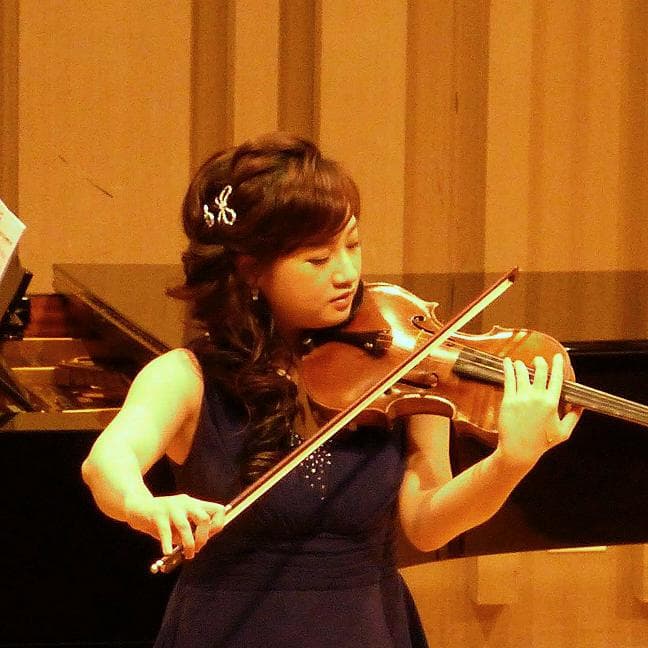 這張照片是一個年輕女孩演奏小提琴的照片。她穿著一件藍色的洋裝,專注地拉著琴,看起來非常投入。