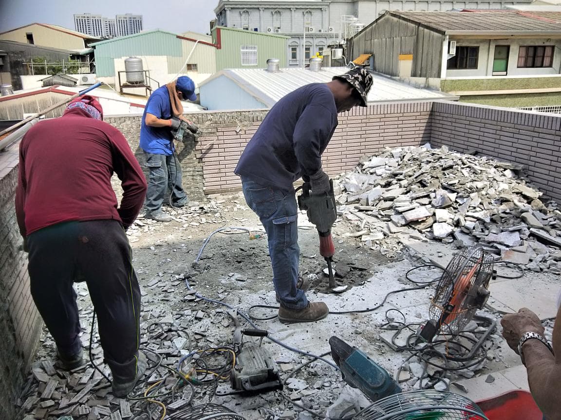 1. 這張照片顯示三個男性站在一片碎石瓦礫之中,他們身穿工作服,其中一人正使用電動工具