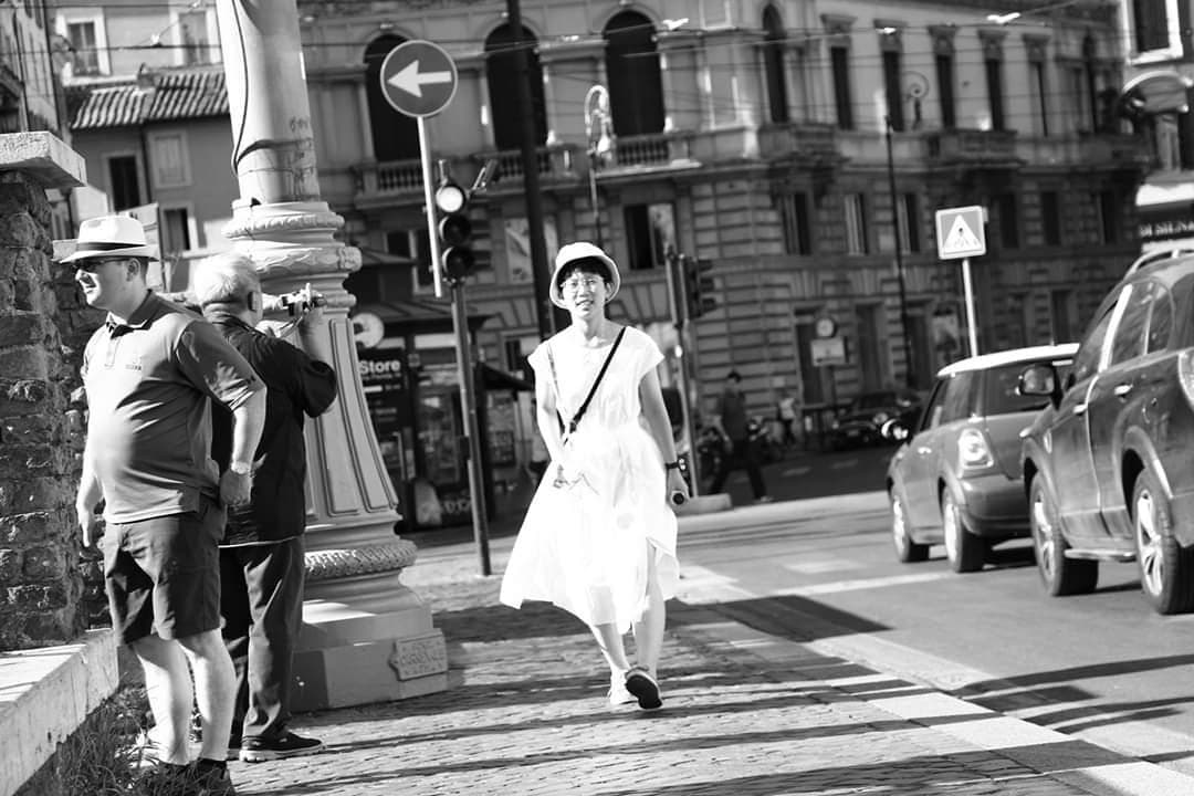 這張「街頭」的照片是一名穿著白色洋裝的年輕女子,她走在街道上,她的左邊有兩位男子,其中一人正在拍照。