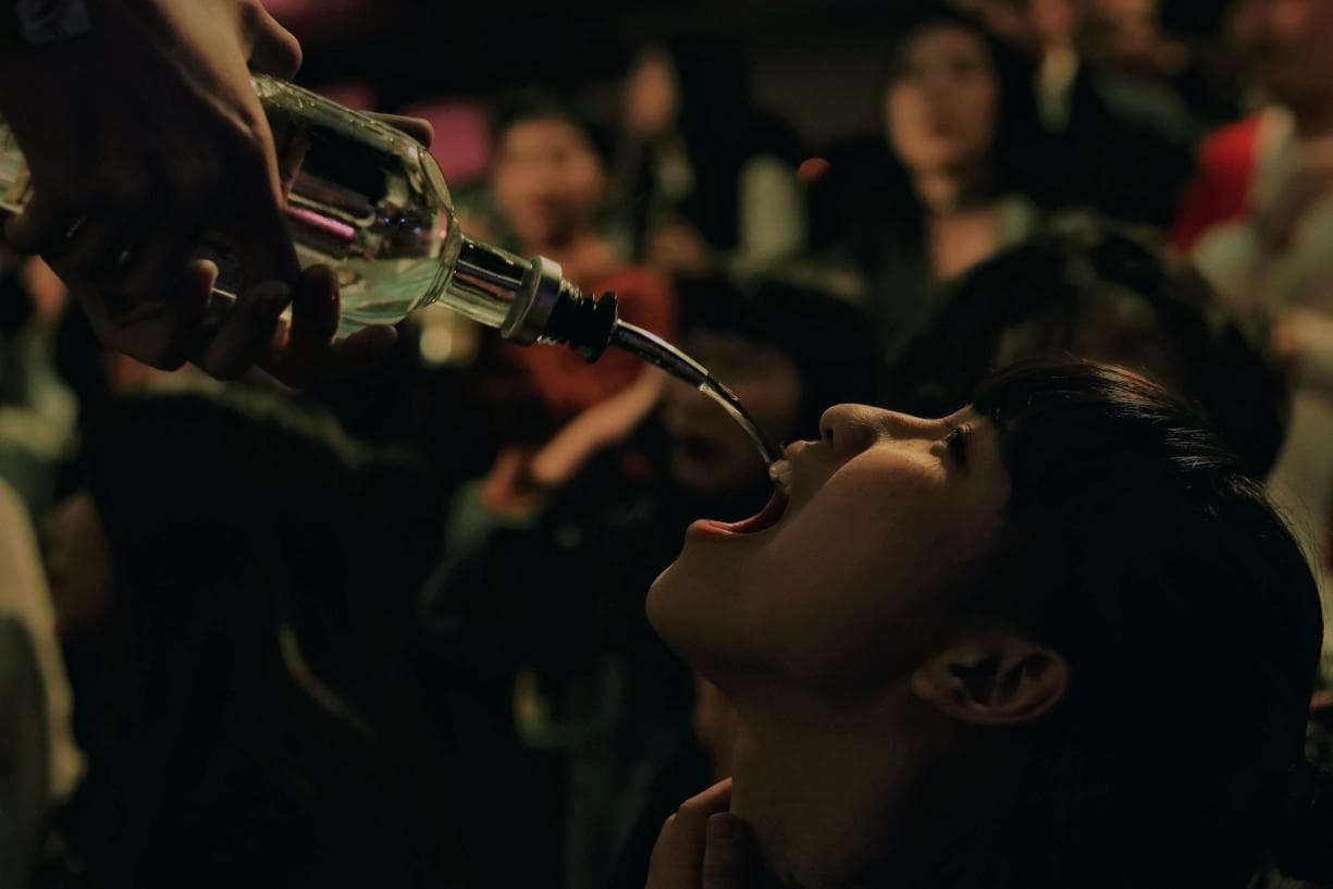 這張「一位女子正從酒瓶中喝酒」的照片是,女子張開嘴,把酒瓶裡的酒灌進嘴巴,畫面中還有許多模糊的人影。