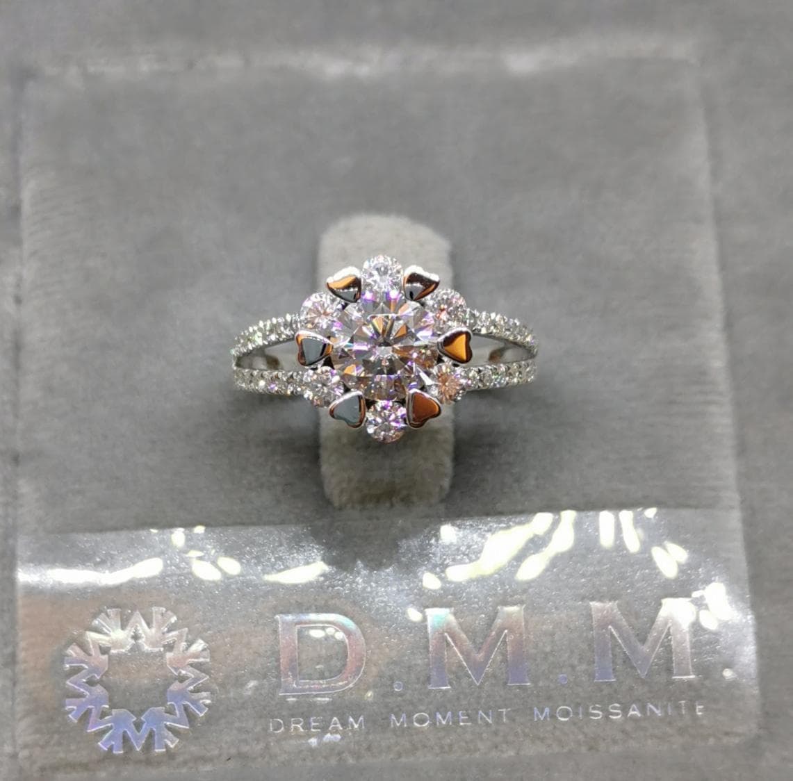 1) 照片顯示一個以鑽石鑲嵌的戒指,戒指上有兩個並排的鑲嵌帶,中央有一個較大的鑽石,周圍環繞著一圈較小的鑽石