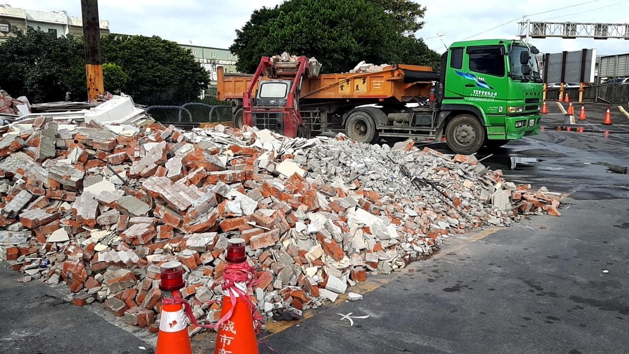 1) 照片中顯示一輛綠色卡車停在道路旁,卡車後面是一堆廢棄的磚塊
