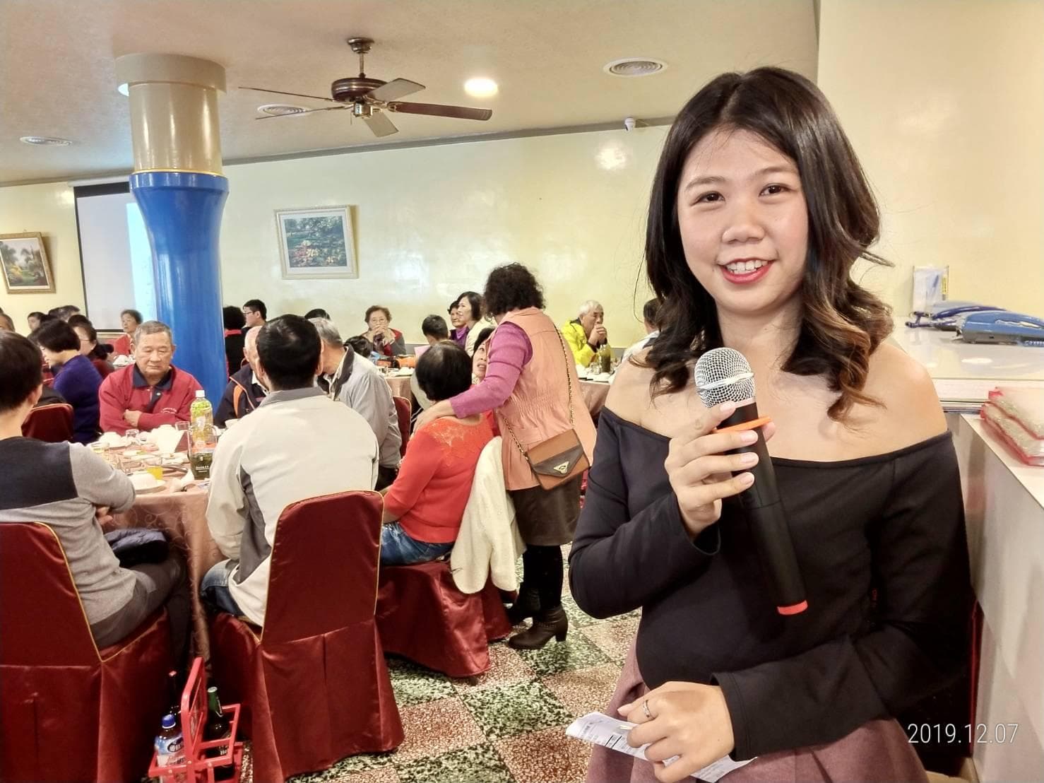 這張「婚宴」的照片是一個年輕女子拿著麥克風在臺上講話,臺下是許多賓客。