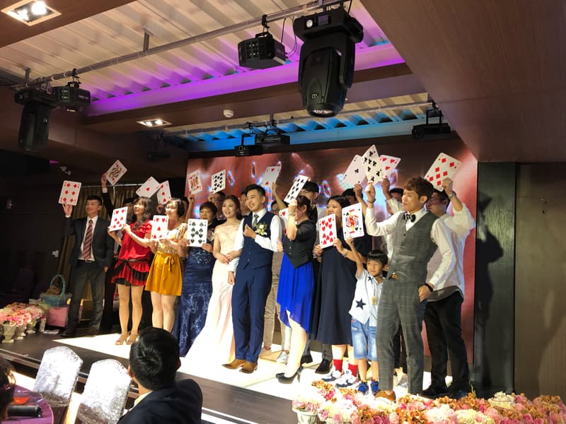 這張「婚禮」的照片是 一群人舉著撲克牌拍照,新娘穿著白色禮服,新郎穿著黑色西裝,大家都很開心。