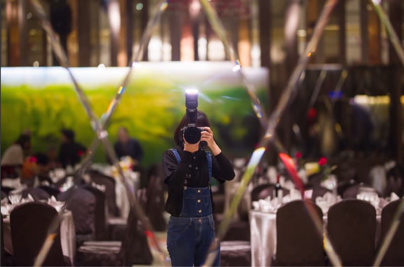 這張「婚禮攝影師」的照片是一個婚禮攝影師在婚禮現場拍攝的照片,他正舉著相機,並用閃光燈拍攝。