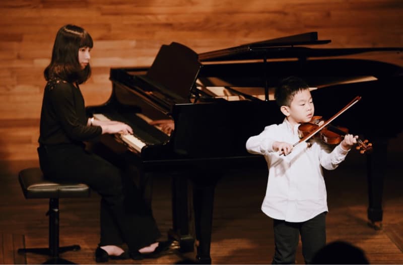 這張「音樂演出」的照片是一位年輕的男孩正在演奏小提琴,一位女性則在鋼琴上伴奏。