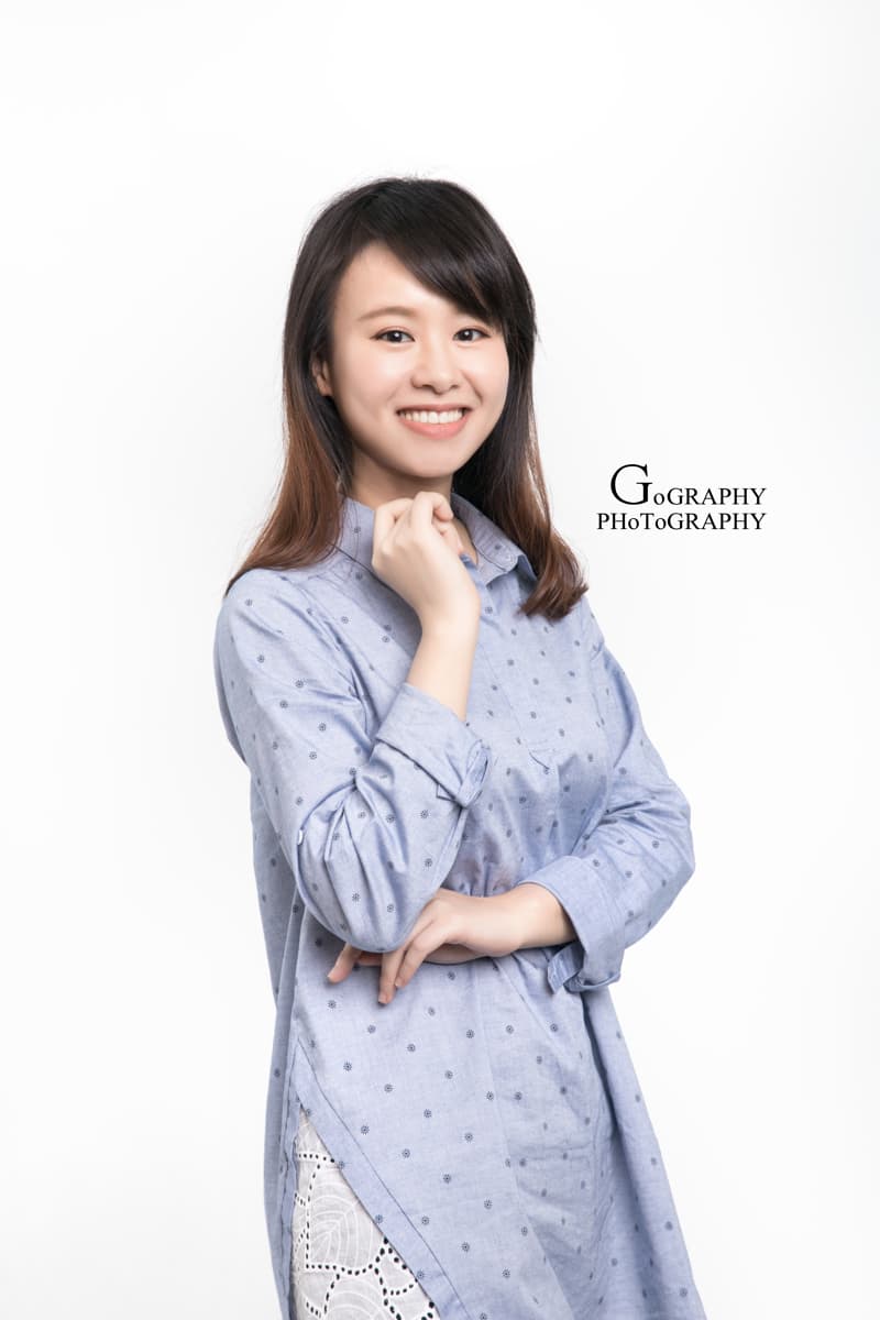 這張「女性肖像」的照片是一個年輕女性,她穿著一件藍色印花襯衫,微笑著看著鏡頭,手放在胸前。