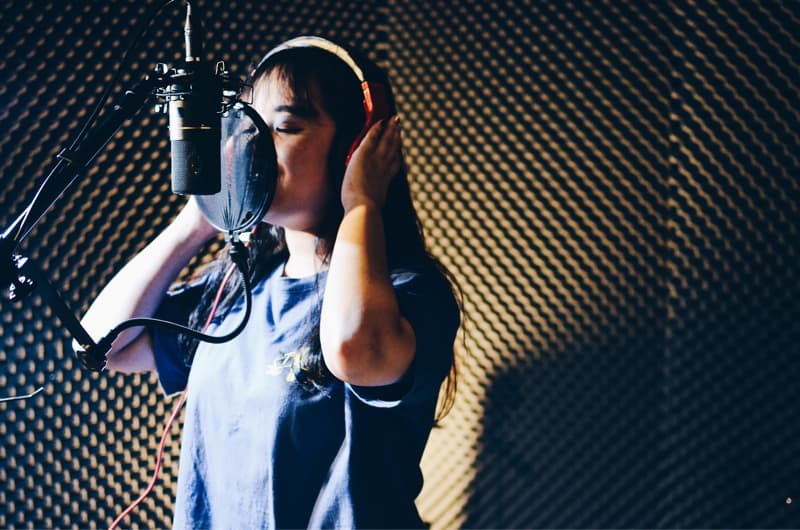 這張「女生在錄音室唱歌」的照片是一個女生戴著耳機,正對著麥克風唱歌。她閉著眼睛,專注地唱歌。