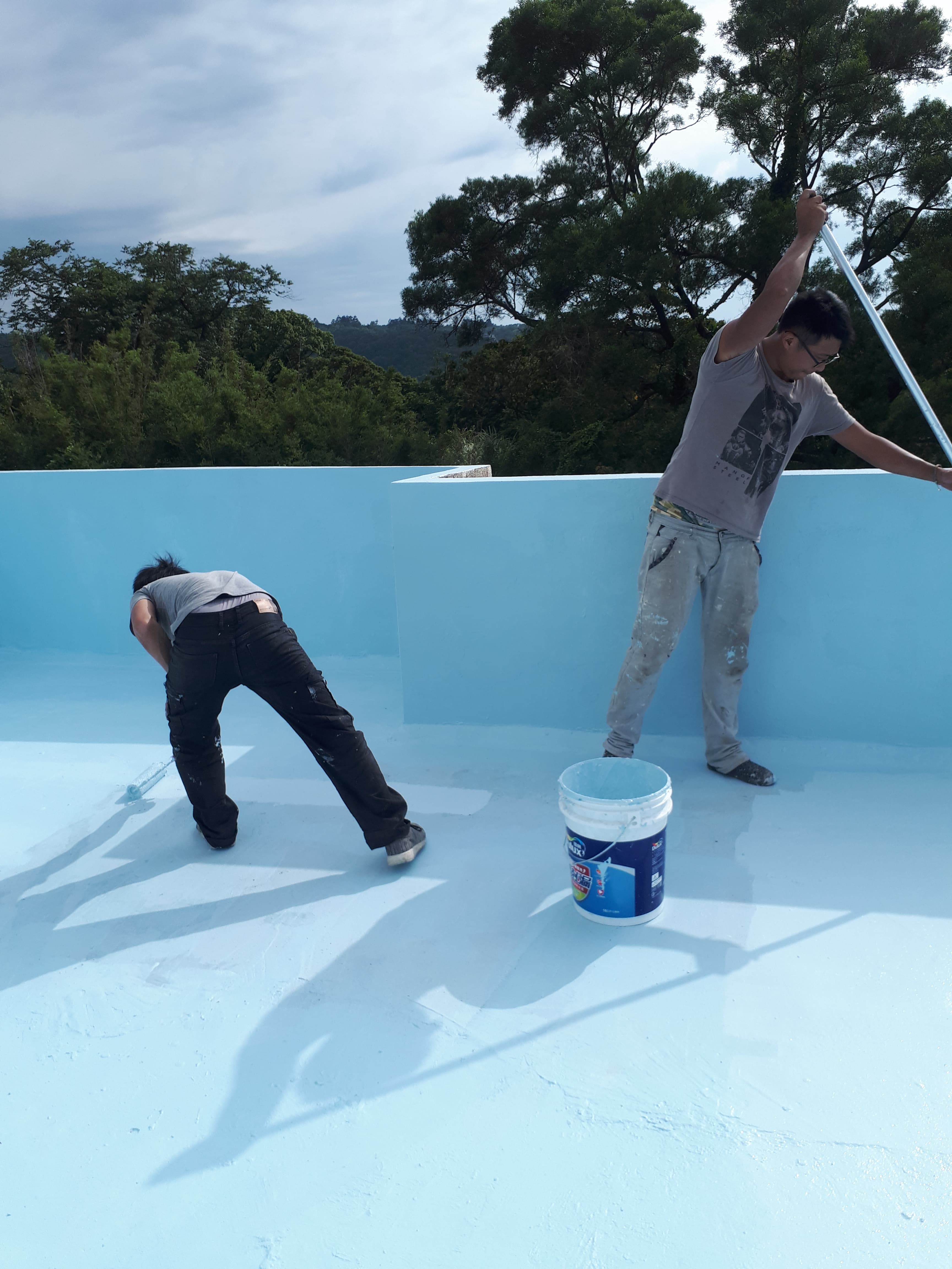 1) 照片中顯示兩位男子正在用刷子粉刷游泳池,其中一人正在使用一個藍色桶子裝水
