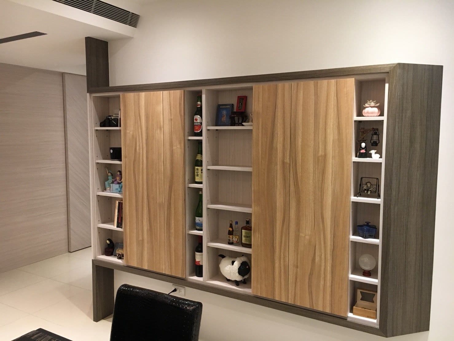 1) 照片顯示一個木質壁櫃,壁櫃有許多層架,架上擺放著許多物品,像是酒瓶、擺飾和書籍