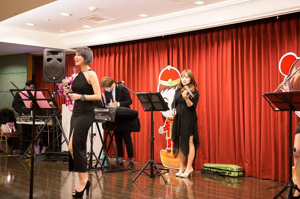 這張「舞臺表演」的照片是四個音樂家在舞臺上演奏,他們身穿正式服裝,背景是紅色布幕,臺上還有卡通人物裝飾。