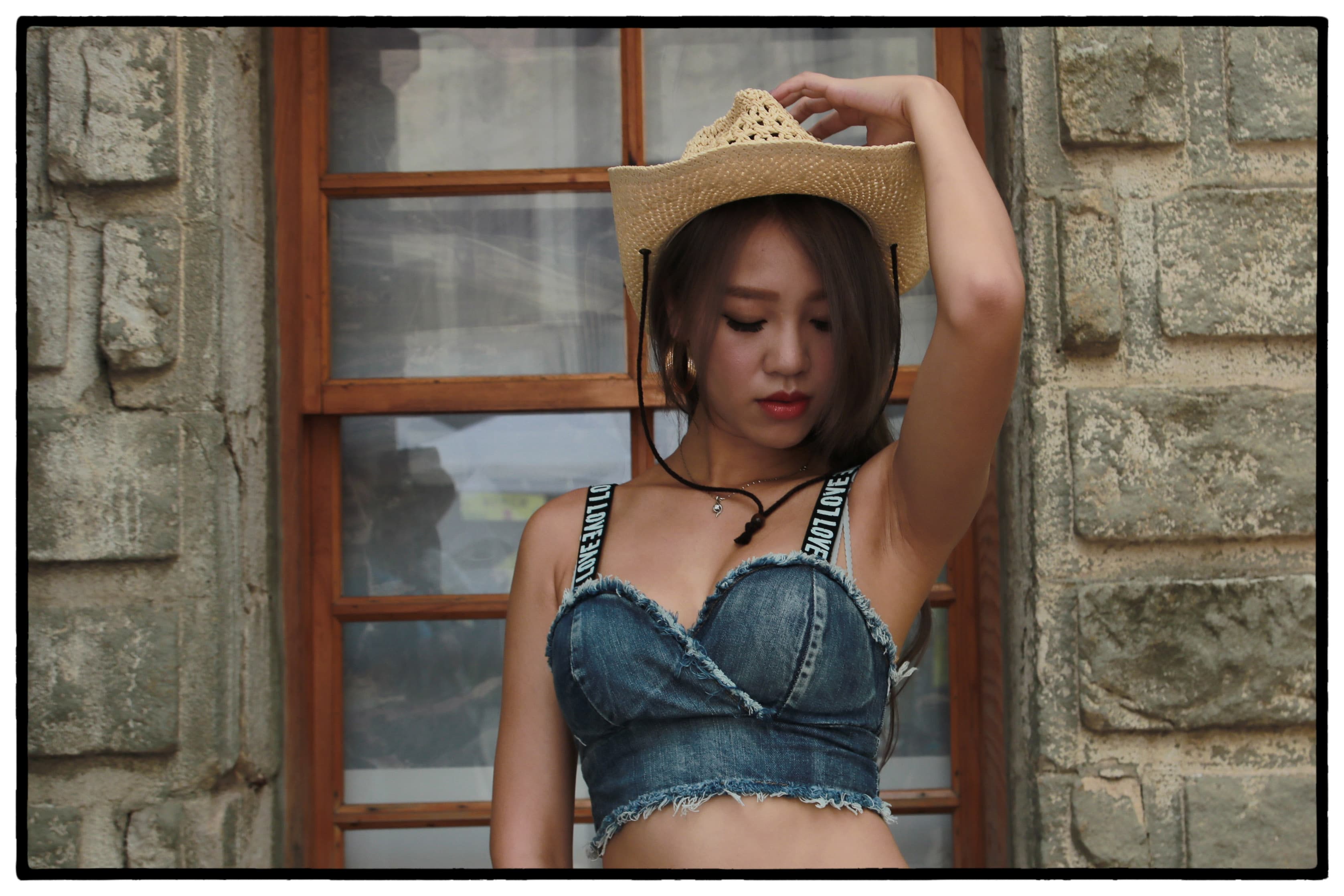 這張照片是一個戴著草帽的女孩,她穿著一件牛仔布的露肩上衣,她的表情有點害羞,顯得非常性感。