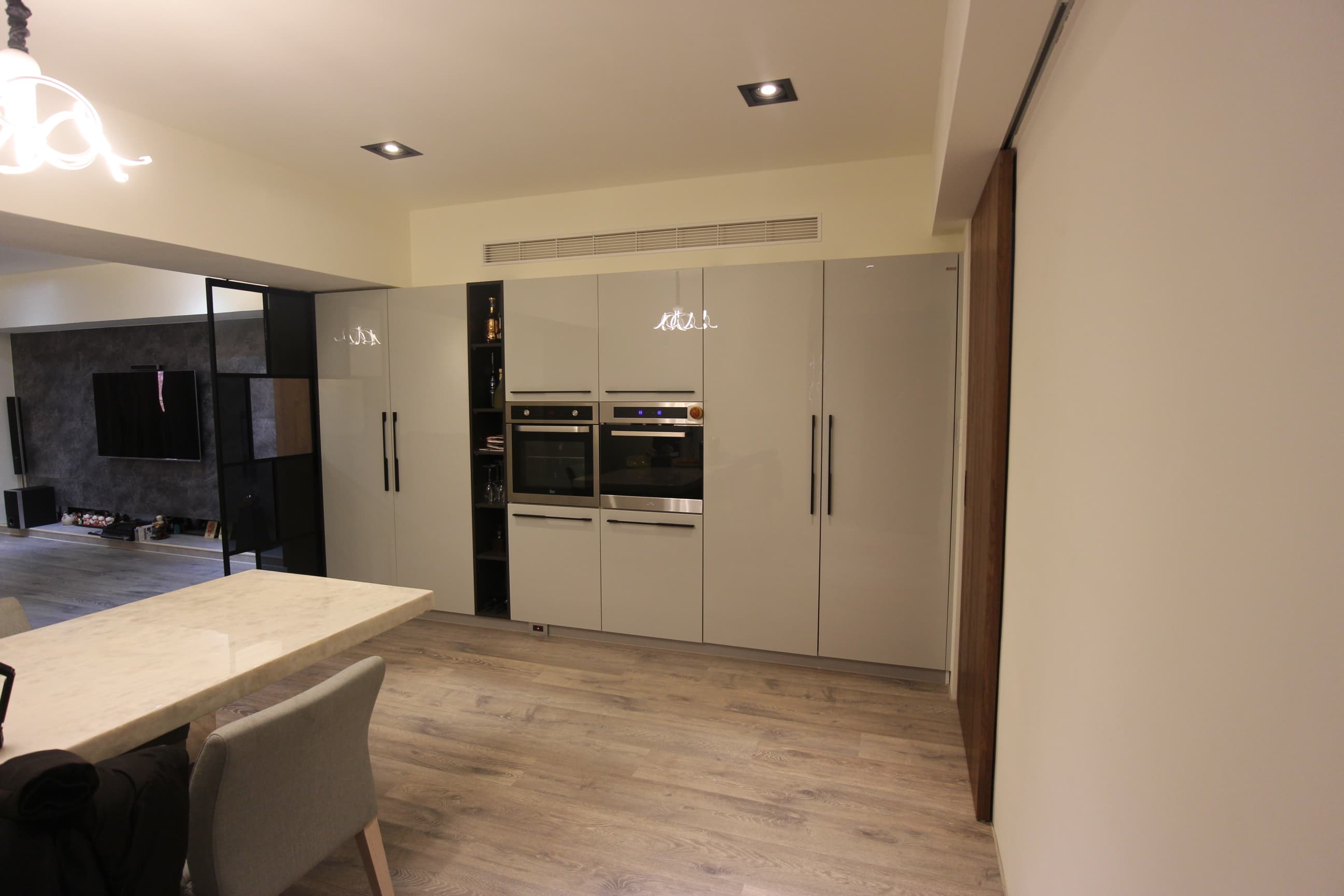 這張照片是一間現代化的廚房,最重要的是牆上整齊排列的白色櫥櫃和烤箱。櫥櫃光滑明亮,烤箱也散發出高級感,整個廚房看起來簡潔乾淨。