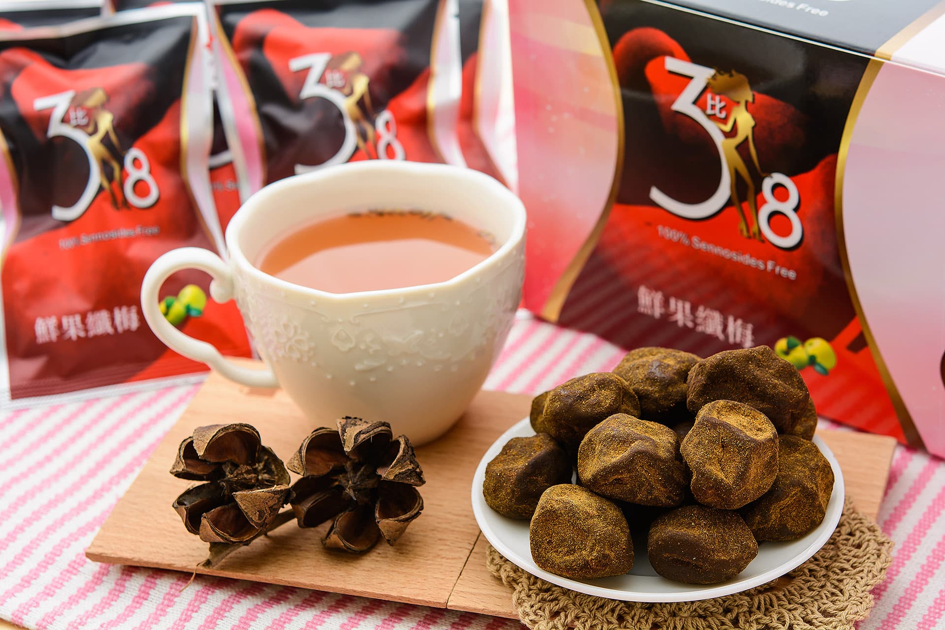 這張「茶與糖果」的照片是,一個白色杯子裝著熱茶,旁邊放著一盒包裝精美、印有數字「38」的糖果。