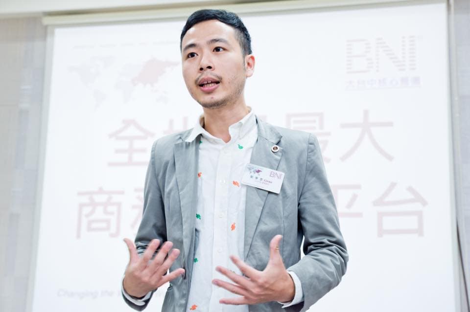 這張照片是一個穿著灰色西裝的年輕男子,他正在發表演講。他的背景是一個白板,上面寫著「全球商務平臺」的字樣。