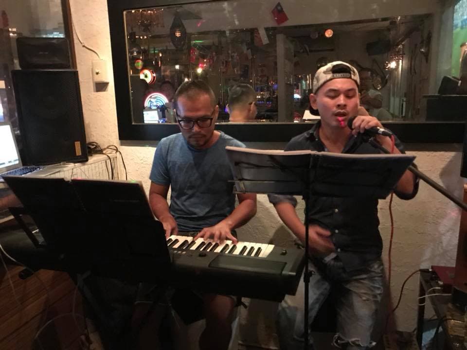 這張「兩個男人在室內演奏音樂」的照片是,其中一個男人正在彈奏電子琴,另一個男人則拿著麥克風唱歌。