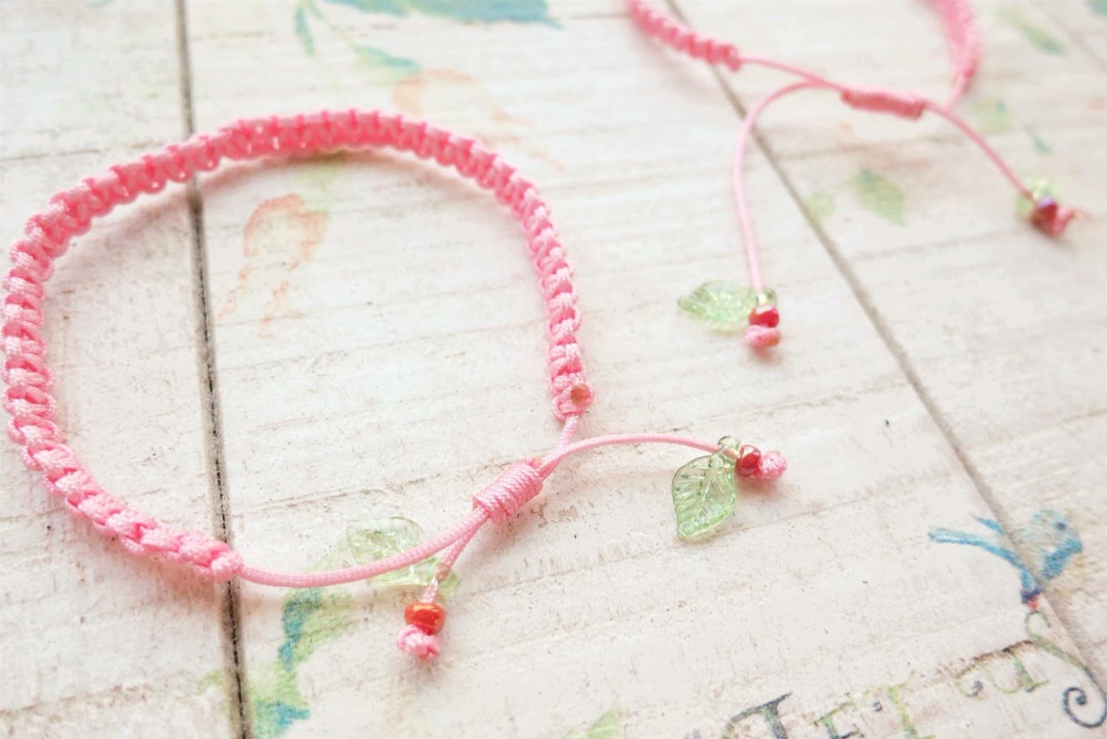 這張「粉紅色繩子手環」的照片是兩條手環,都有葉子形狀的裝飾。
