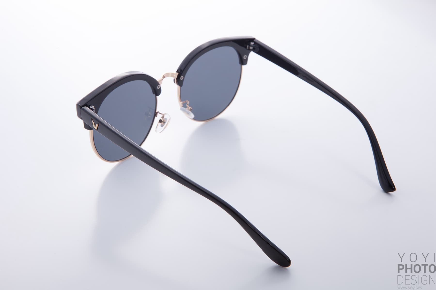 這張照片是一副黑色的太陽眼鏡,鏡框呈半圓形,鏡片是深色的,鏡架上有一個金色的 V 形標誌。