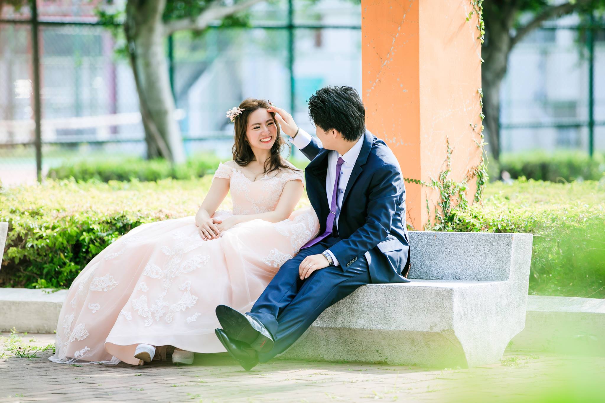 這張照片是一對新人在戶外拍攝婚紗照,畫面中男方正輕輕地撫摸著女方的頭,女方則露出幸福的笑容,兩人甜蜜的互動充滿著愛意,展現了新婚的喜悅和幸福。