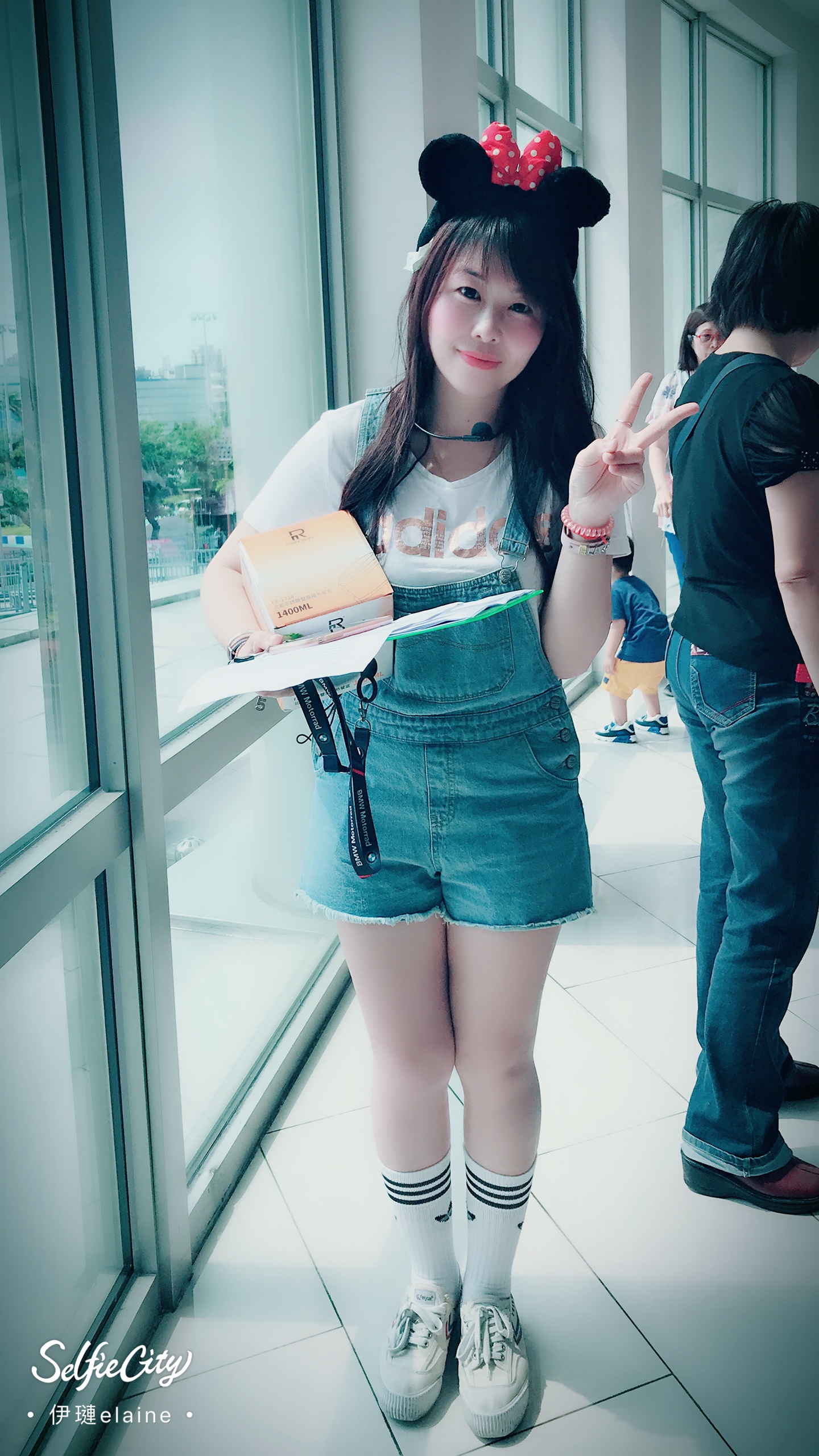 這張照片是一個穿著米奇老鼠耳朵的年輕女孩,她拿著一個盒子,她看起來很開心,背景是一個明亮的房間。