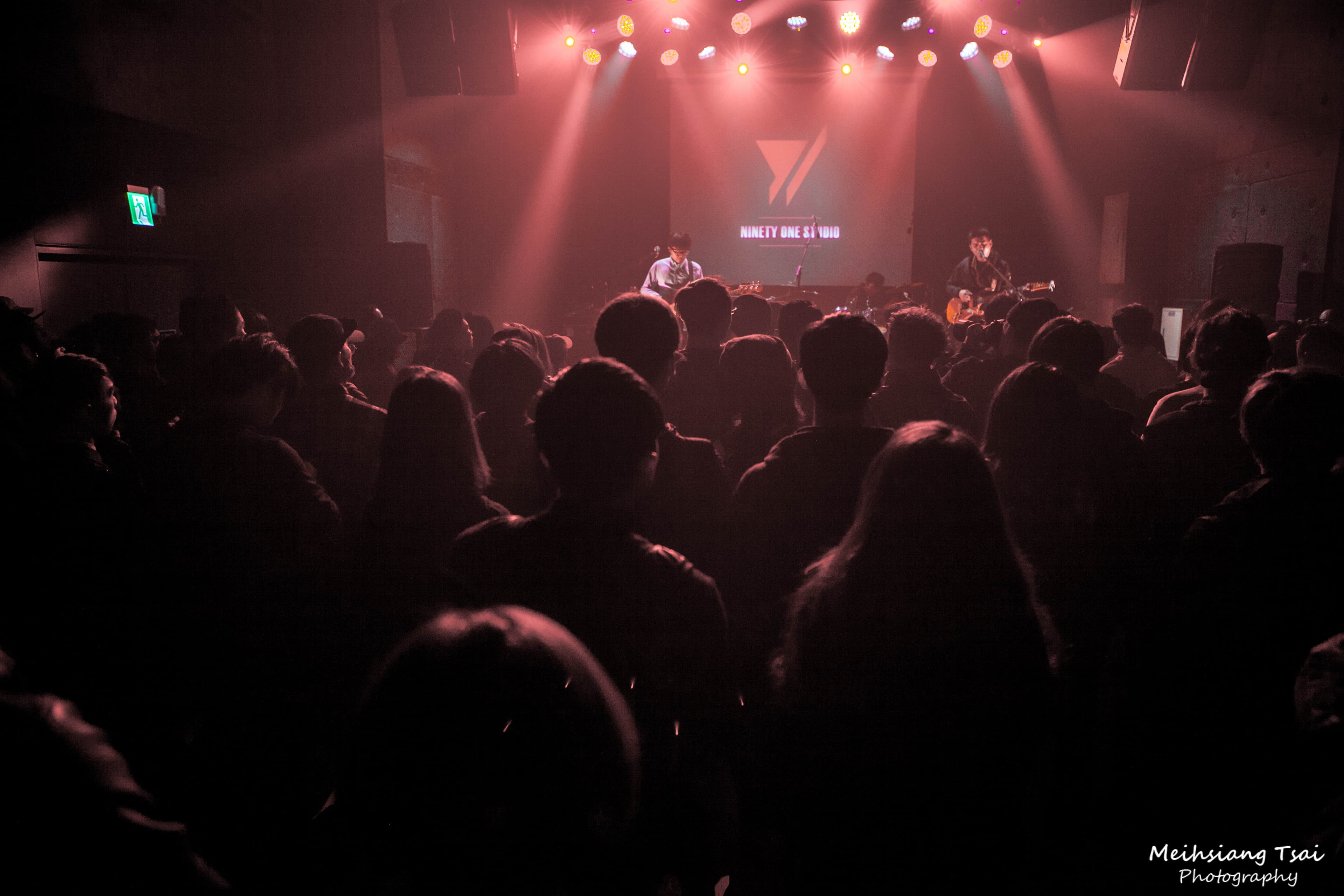 1) 這是一張在黑暗的演唱會場地中拍攝的照片,場地裡擠滿了觀眾,舞台上有一位歌手正在表演,但歌手被觀眾擋住了