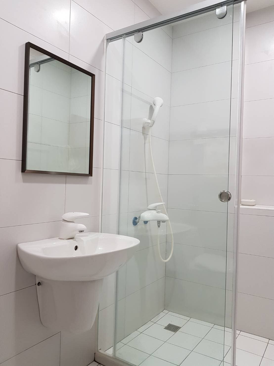 這張照片是一個現代化的浴室,最主要的部分是浴室的淋浴間,淋浴間的玻璃門上有兩個把手,淋浴間的牆壁上裝有一個白色的淋浴頭,淋浴間的地板上有一個白色的地漏。