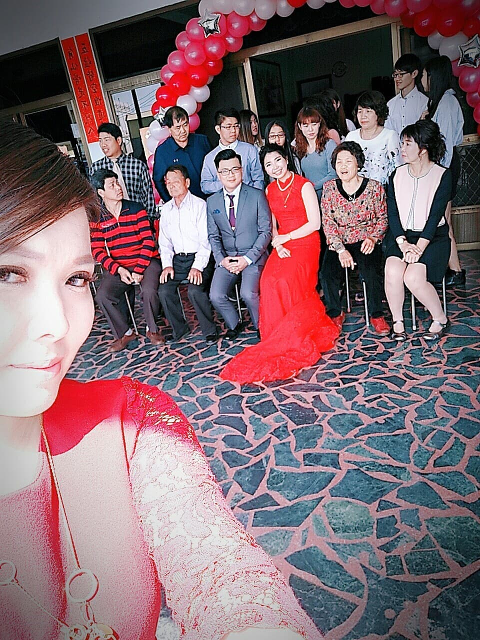 這張「婚禮」的照片是一個新郎新娘和賓客們的合照。新郎穿著西裝,新娘穿著紅色禮服,他們在中間,旁邊是親朋好友,還有許多紅色氣球裝飾著背景。