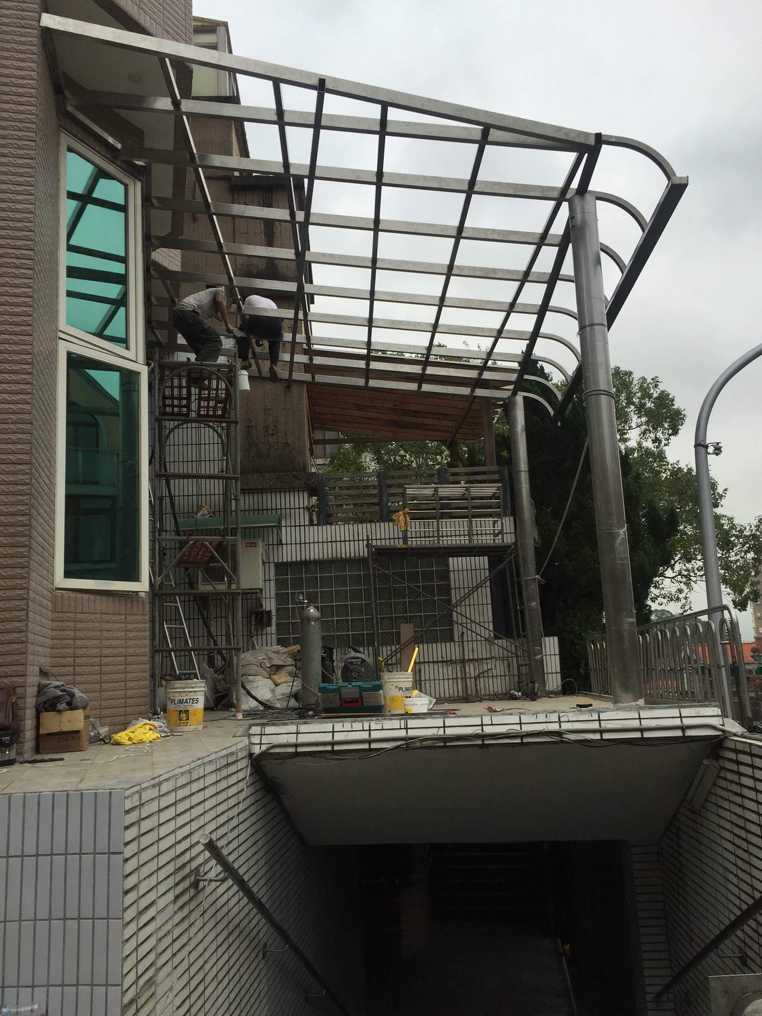 1) 照片顯示一棟建築物的外觀,建築物上方有鐵製的遮雨棚,遮雨棚下有堆積的雜物,以及一輛小型貨車