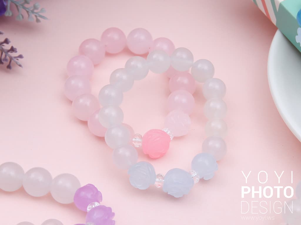 這張照片是兩條粉紅色和白色的珠子手鍊,它們放在粉紅色的背景上,中間有一顆粉紅色的珠子,非常可愛。