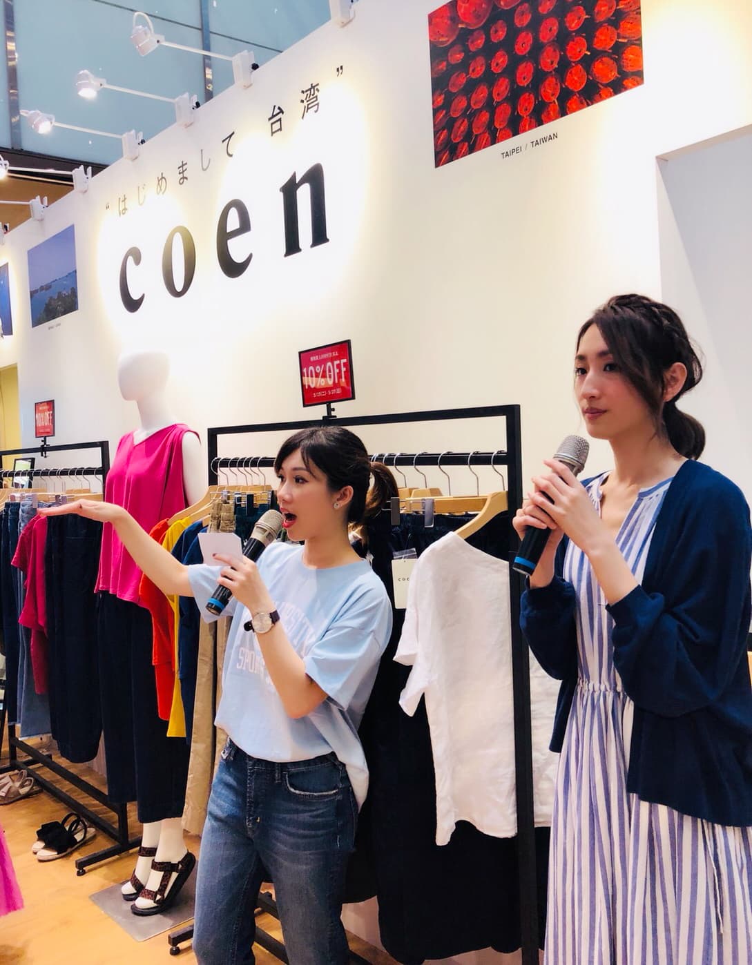 這張「服裝店」的照片是一個在店內舉辦活動的場景,照片中兩位女性正在舞臺上介紹服裝,舞臺的背景是服裝店招牌和商品展示區。