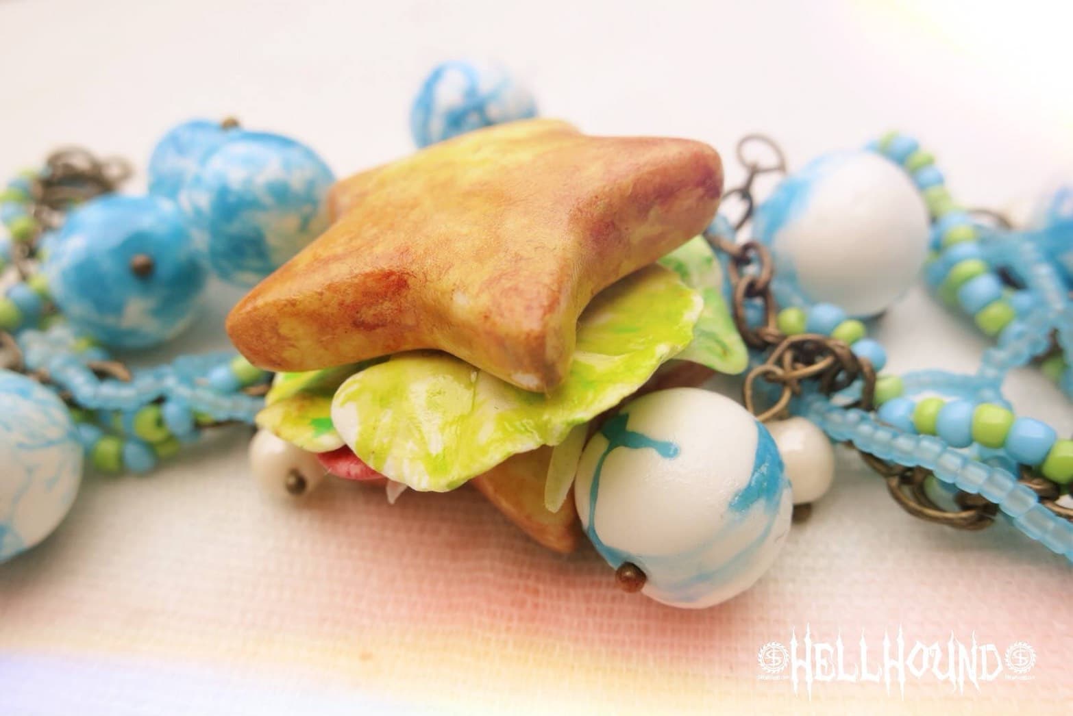 這張「星形三明治」的照片是一個用模型製作的三明治,上面有綠色的生菜和白色的奶油,下面是褐色的麵包,旁邊放著藍色、白色、綠色的串珠。