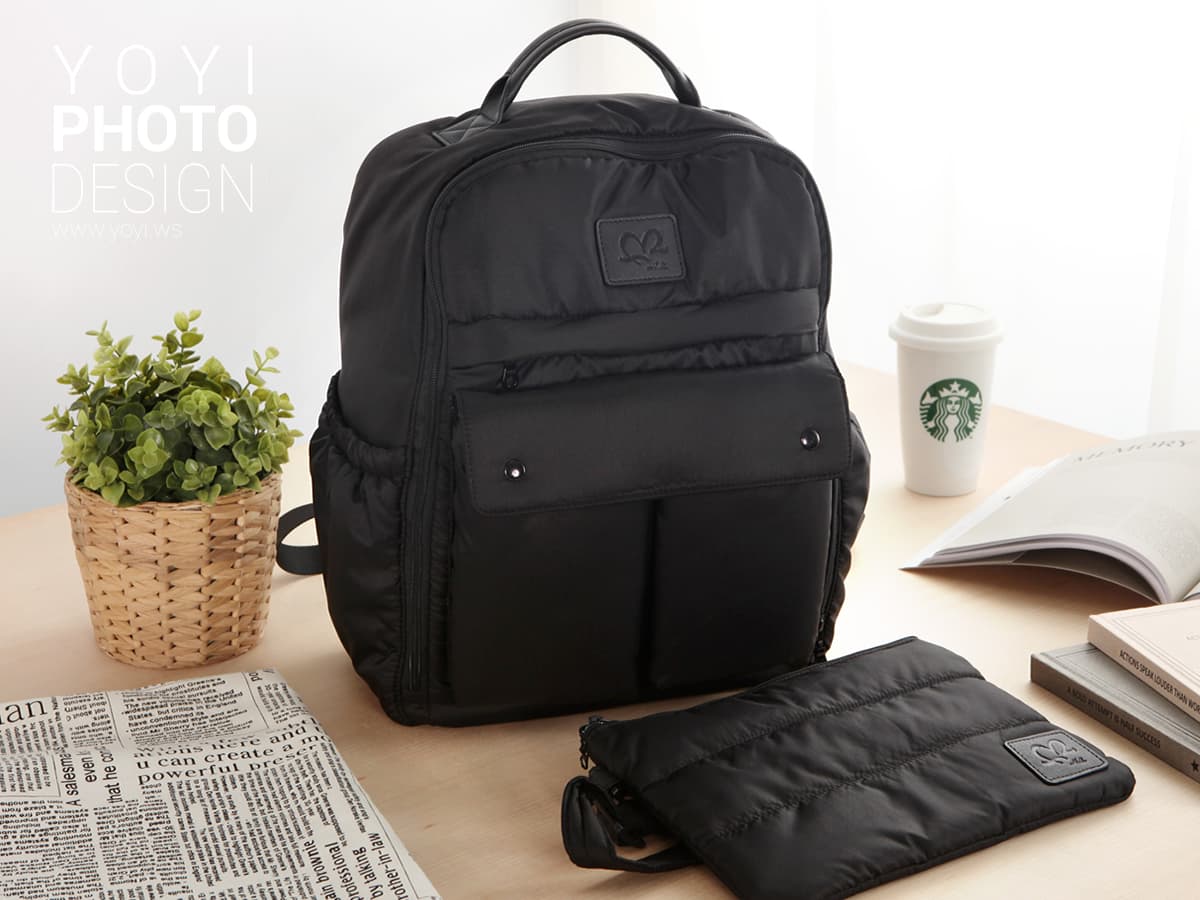 這張「黑色後揹包」的照片是,包包放著一個黑色小包,旁邊有一盆綠色植物。