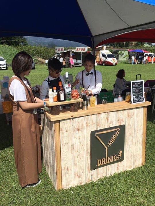 這張照片是一個木製的流動酒吧,上面有一個綠色的招牌,上面寫著「MEOW DRINK」。